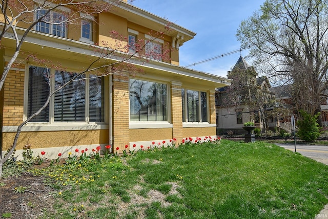 view of property exterior with a yard, brick siding, and stucco siding