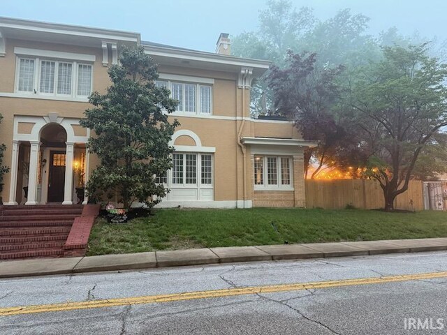 view of front of property with a chimney, a front yard, stucco siding, and fence