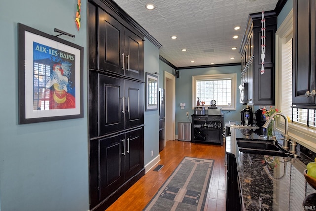 kitchen with wood finished floors, dark stone countertops, a sink, crown molding, and stainless steel microwave