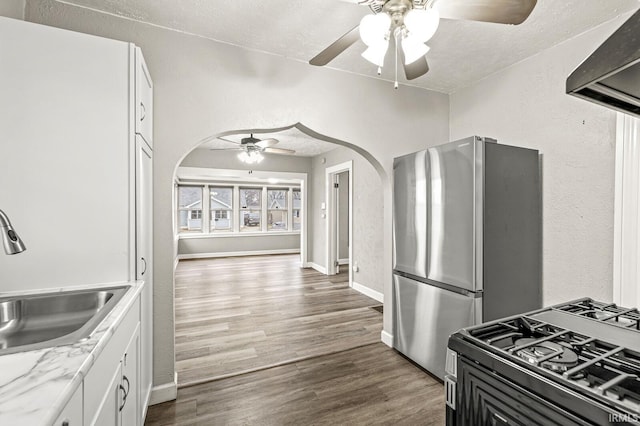 kitchen with freestanding refrigerator, ceiling fan, arched walkways, a sink, and wood finished floors