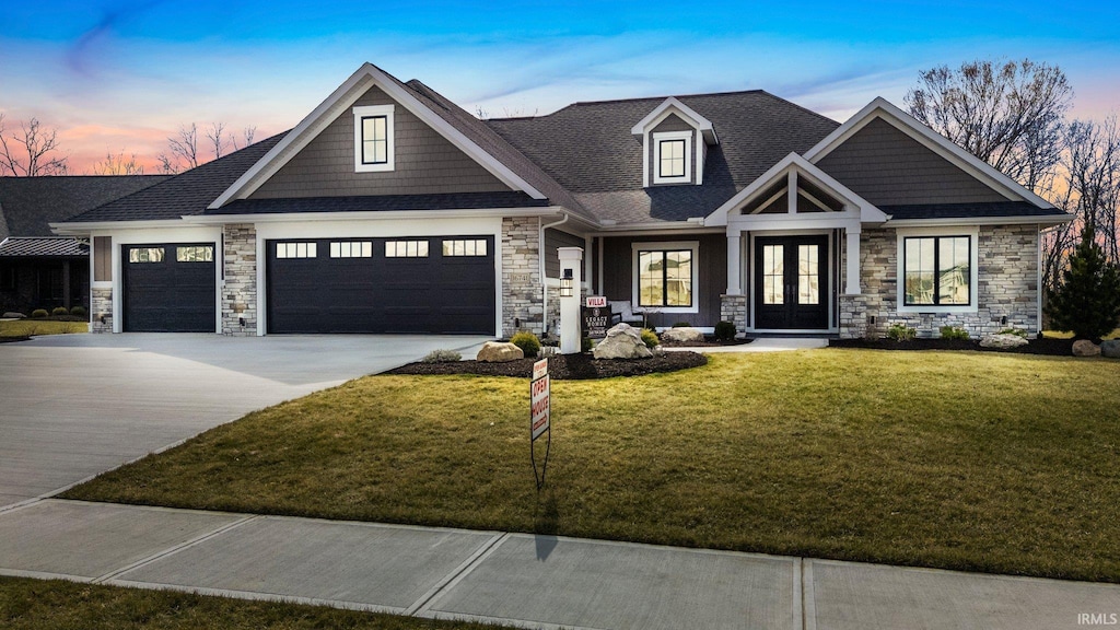 craftsman house with an attached garage, french doors, stone siding, driveway, and a front lawn
