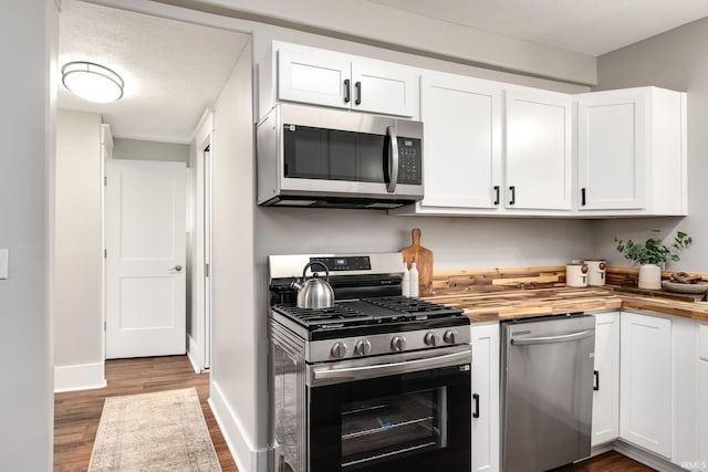 kitchen with white cabinets, appliances with stainless steel finishes, wood counters, and wood finished floors
