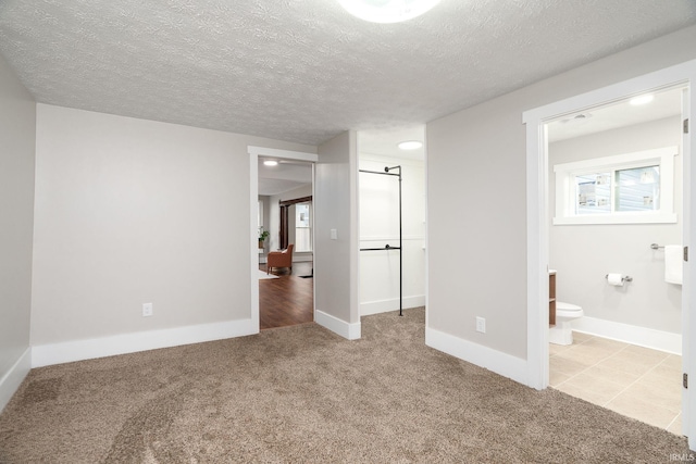 unfurnished bedroom featuring baseboards, carpet flooring, a textured ceiling, and ensuite bath