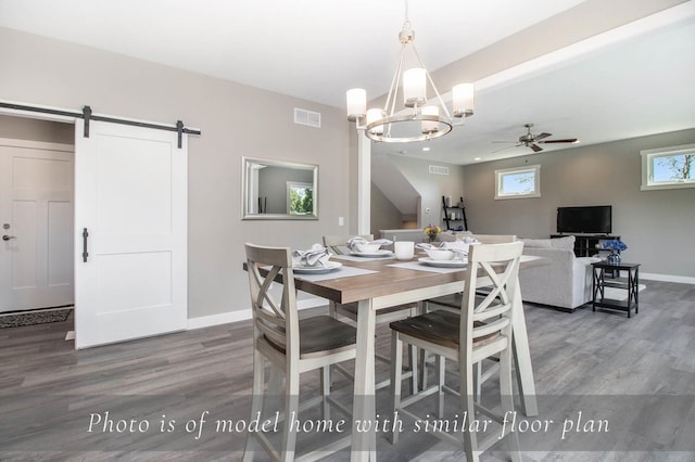 dining area with ceiling fan with notable chandelier, visible vents, a barn door, wood finished floors, and baseboards