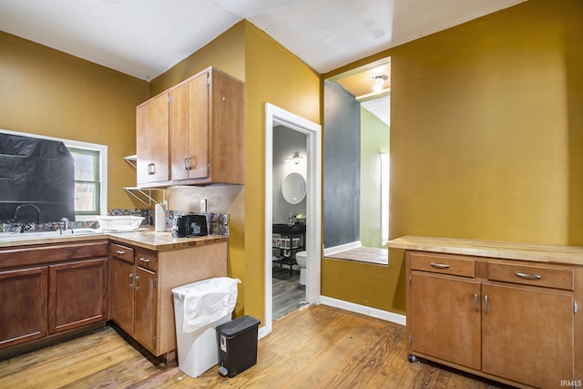 kitchen featuring baseboards, brown cabinetry, light wood-style flooring, and a sink