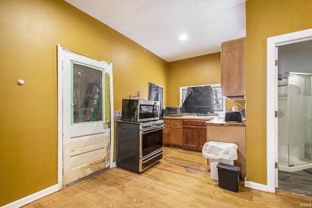 kitchen with a sink, brown cabinetry, stainless steel microwave, baseboards, and light wood-style floors