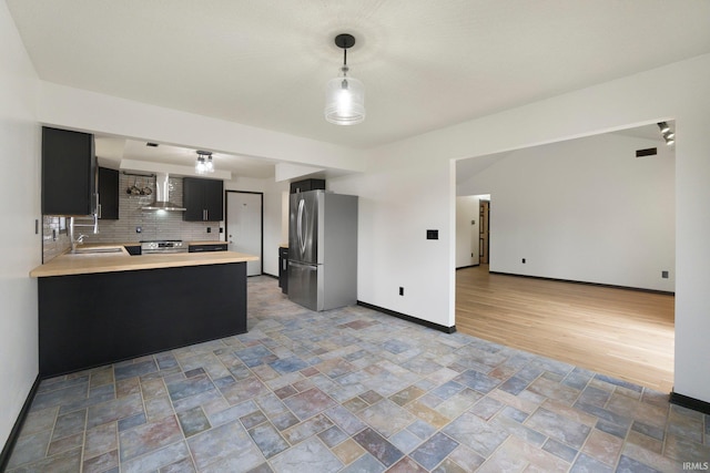 kitchen with light countertops, backsplash, wall chimney exhaust hood, dark cabinetry, and appliances with stainless steel finishes