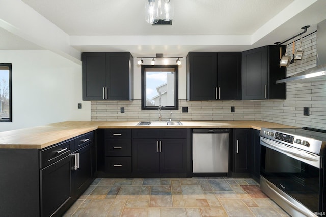 kitchen with stainless steel appliances, backsplash, wooden counters, a sink, and a peninsula