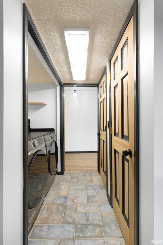corridor featuring a textured ceiling, washer and clothes dryer, and stone finish flooring
