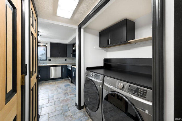 laundry room featuring cabinet space, stone finish floor, washing machine and dryer, and a textured ceiling