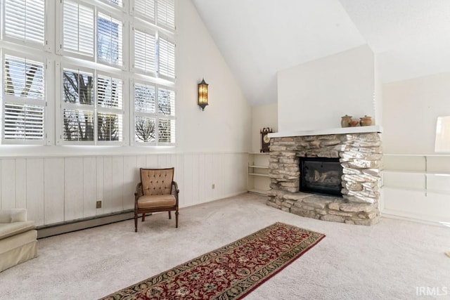 living area featuring high vaulted ceiling, carpet flooring, a stone fireplace, a baseboard radiator, and wainscoting