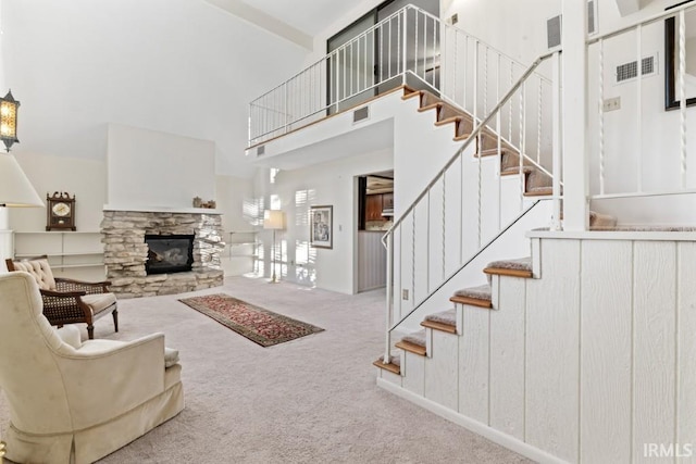 carpeted living area with stairs, a towering ceiling, visible vents, and a stone fireplace