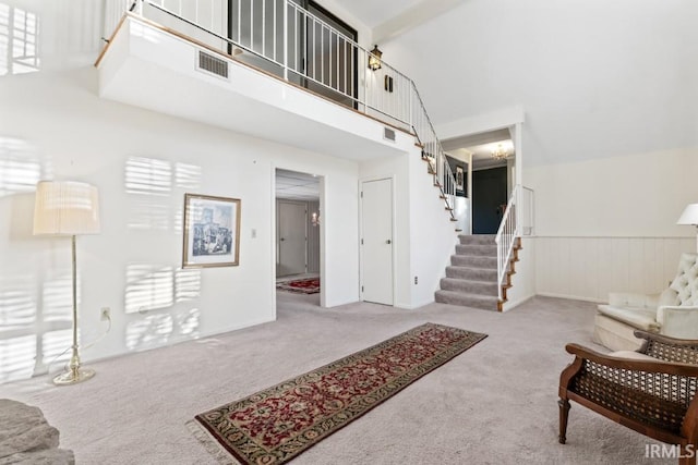 living room with carpet flooring, a towering ceiling, visible vents, and stairs