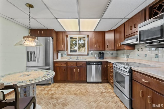 kitchen with light countertops, appliances with stainless steel finishes, under cabinet range hood, a sink, and backsplash