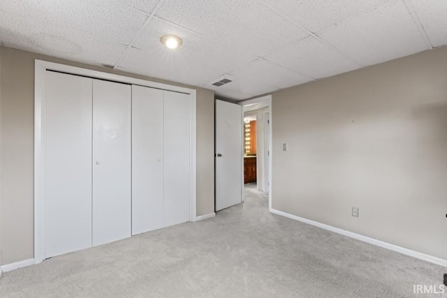unfurnished bedroom featuring a closet, baseboards, light colored carpet, visible vents, and a paneled ceiling