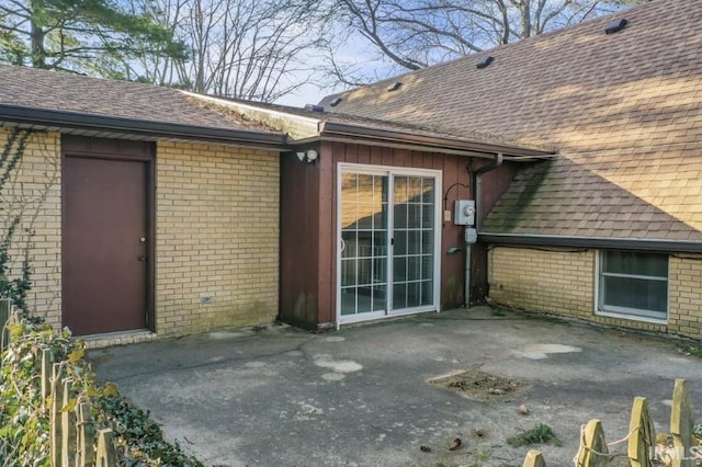 exterior space with a shingled roof, a patio, and brick siding
