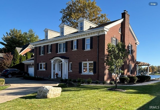 colonial-style house featuring a chimney, a garage, brick siding, a front lawn, and driveway