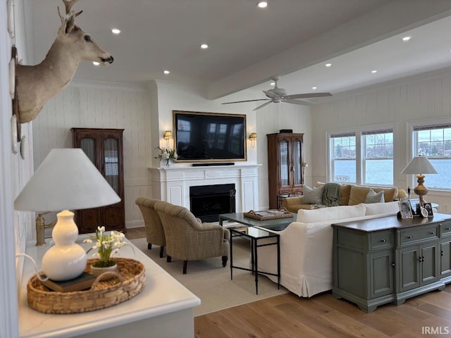 living area with crown molding, light wood finished floors, a fireplace, ceiling fan, and beam ceiling
