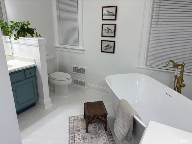 bathroom featuring vanity, a freestanding tub, toilet, baseboards, and visible vents