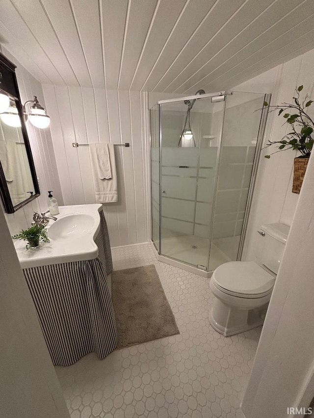 bathroom with a shower stall, toilet, wood walls, and vanity