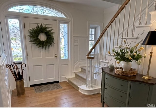 foyer entrance with a wealth of natural light, a decorative wall, stairway, and light wood finished floors