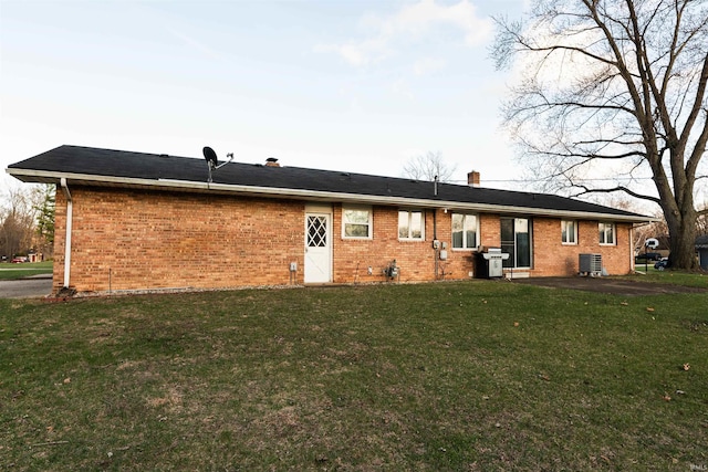 rear view of property with brick siding, a chimney, cooling unit, and a yard