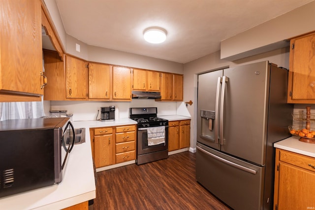 kitchen featuring light countertops, appliances with stainless steel finishes, brown cabinets, under cabinet range hood, and dark wood-type flooring