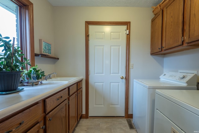 clothes washing area featuring washer and clothes dryer, baseboards, a textured ceiling, a sink, and cabinet space