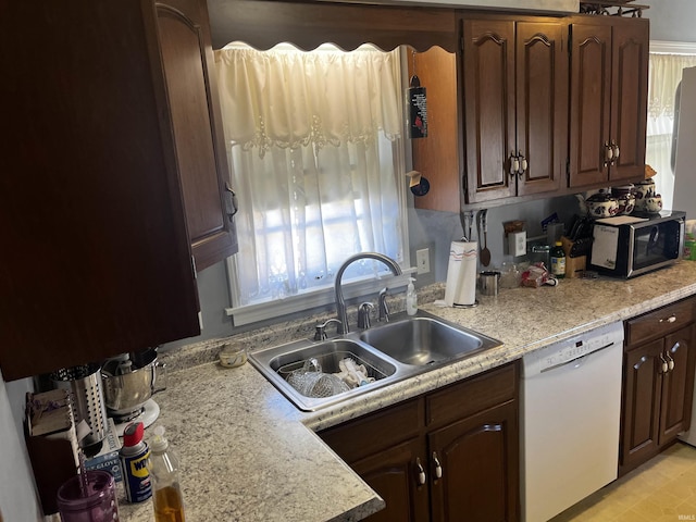 kitchen featuring light countertops, stainless steel microwave, dark brown cabinetry, a sink, and white dishwasher