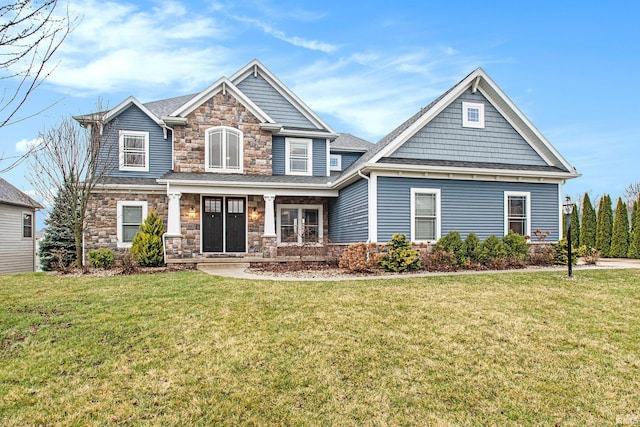 craftsman house with a front lawn, stone siding, and roof with shingles