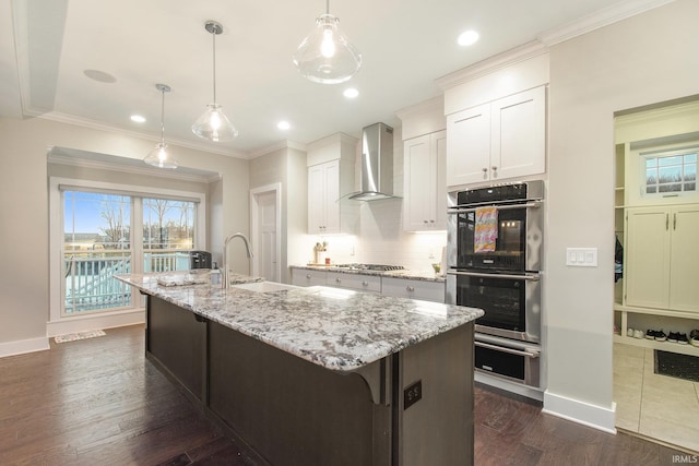 kitchen featuring a sink, a warming drawer, stainless steel appliances, wall chimney range hood, and dark wood-style flooring
