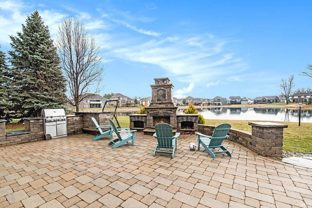 view of patio / terrace with an outdoor stone fireplace, a water view, area for grilling, a residential view, and an outdoor kitchen