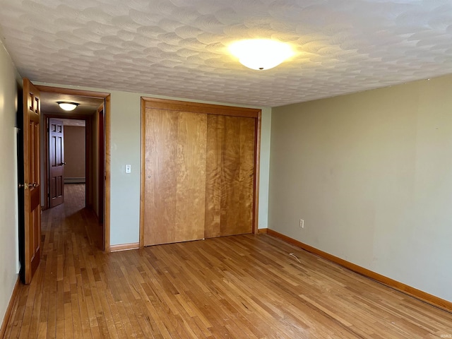 unfurnished bedroom featuring a baseboard heating unit, a textured ceiling, light wood-type flooring, baseboards, and a closet