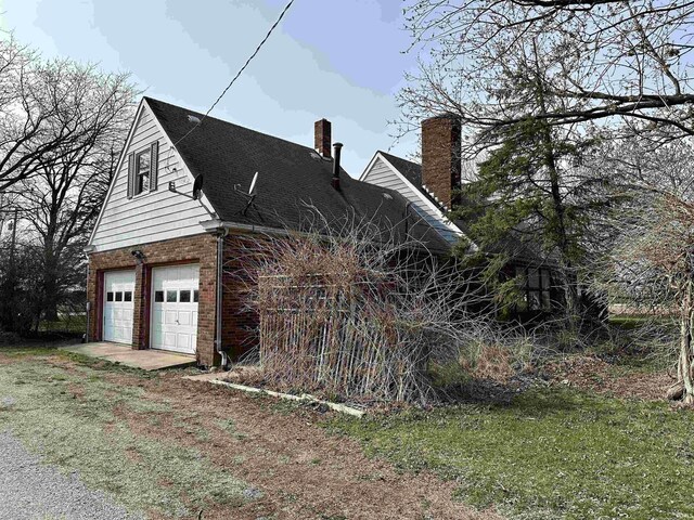 view of side of property with a chimney, brick siding, and a garage