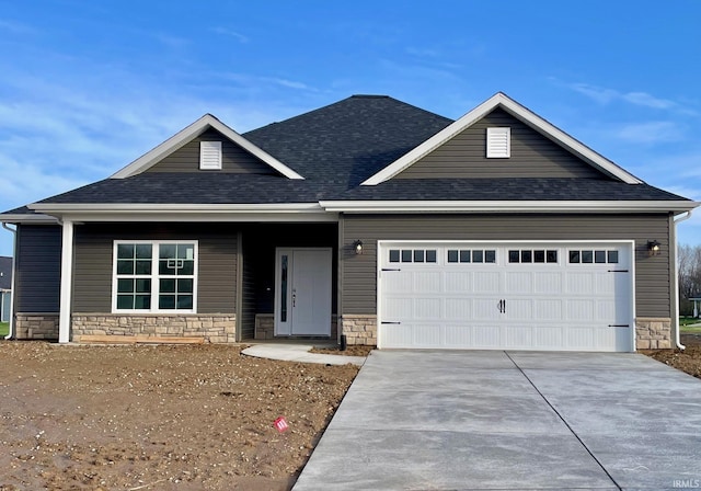 view of front facade with a shingled roof, stone siding, a garage, and concrete driveway
