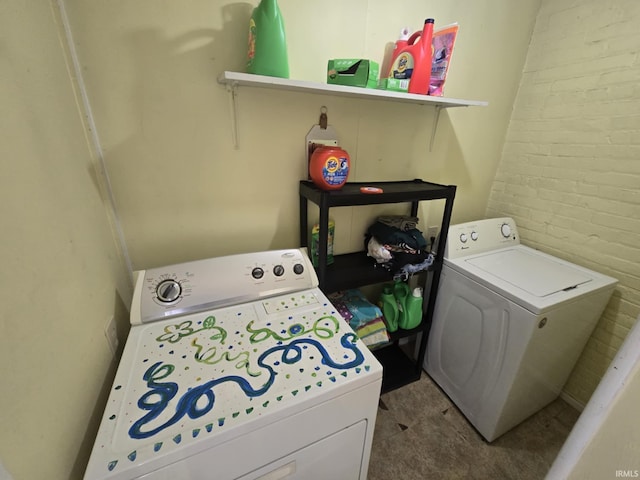 clothes washing area with laundry area, separate washer and dryer, and brick wall