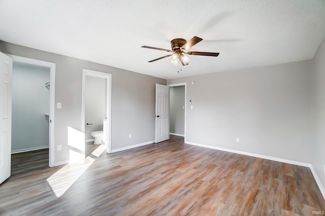 unfurnished bedroom featuring a closet, wood finished floors, a spacious closet, ensuite bathroom, and baseboards