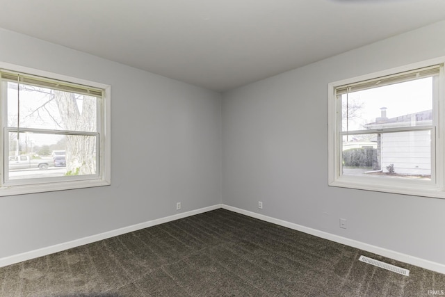 empty room featuring baseboards, dark colored carpet, and visible vents