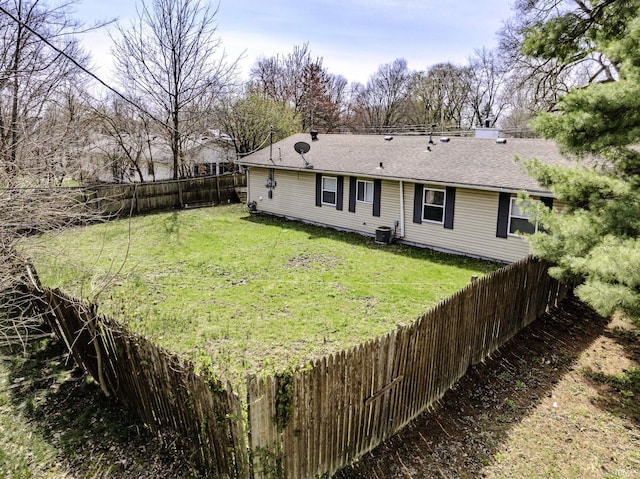 rear view of house featuring roof with shingles, fence private yard, central AC, and a yard
