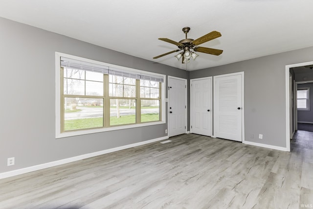 unfurnished bedroom with baseboards, multiple closets, ceiling fan, and wood finished floors