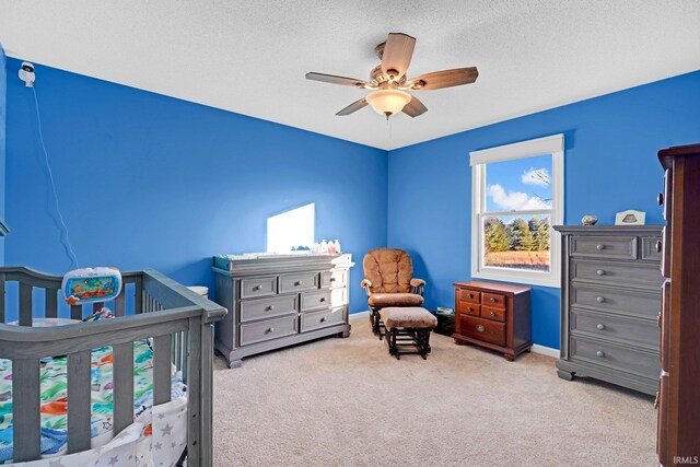 bedroom featuring a crib, light carpet, a textured ceiling, baseboards, and ceiling fan