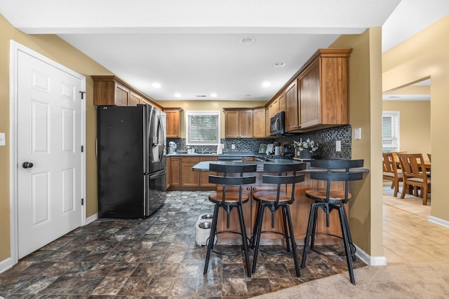 kitchen with backsplash, a kitchen breakfast bar, a peninsula, stainless steel fridge with ice dispenser, and brown cabinetry