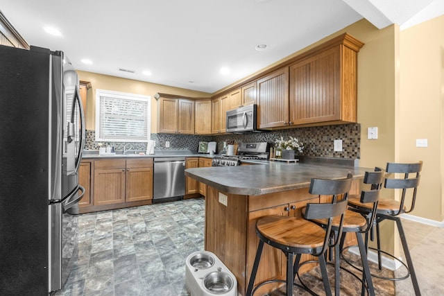 kitchen featuring a peninsula, dark countertops, appliances with stainless steel finishes, and decorative backsplash