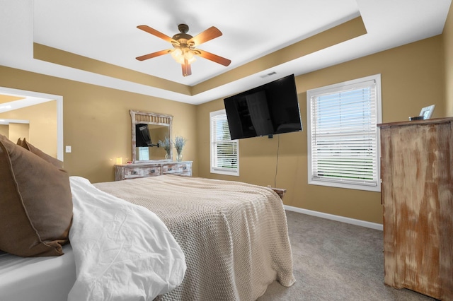 carpeted bedroom with baseboards, a tray ceiling, and ceiling fan