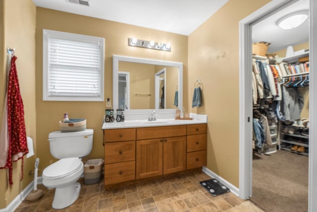 bathroom featuring toilet, vanity, a walk in closet, baseboards, and visible vents
