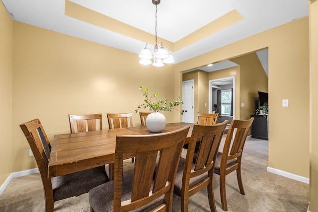 dining area with a tray ceiling, light colored carpet, a notable chandelier, and baseboards