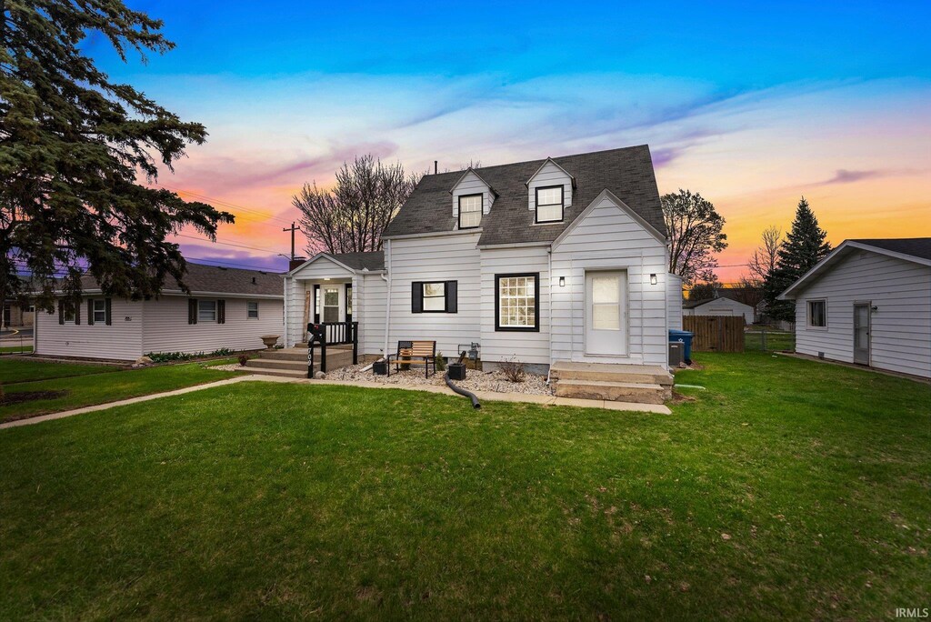 back of property at dusk featuring fence and a lawn