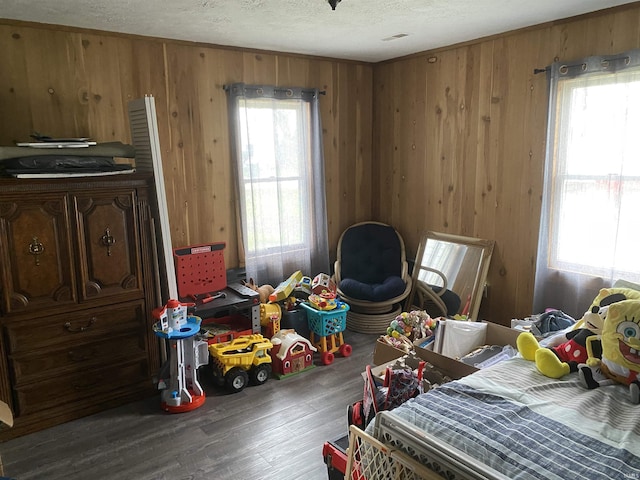bedroom featuring multiple windows, wood finished floors, wood walls, and a textured ceiling