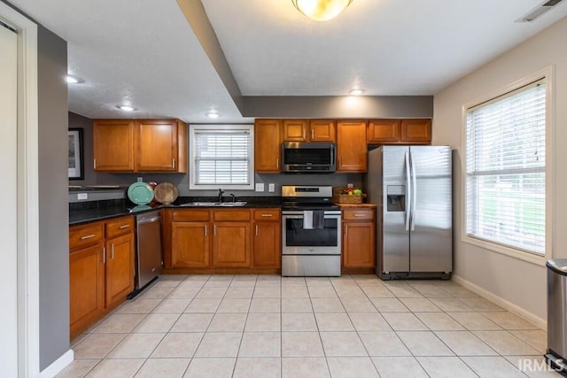kitchen with brown cabinetry, light tile patterned floors, a sink, and appliances with stainless steel finishes