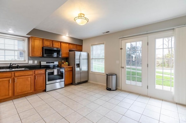 kitchen featuring brown cabinetry, appliances with stainless steel finishes, a sink, and dark countertops